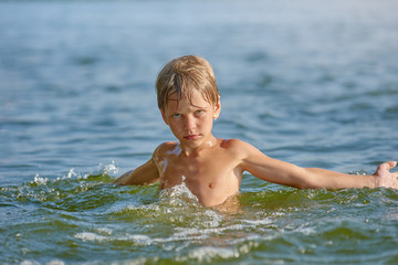 Portrait of young serious boy swimming in the lake at summer