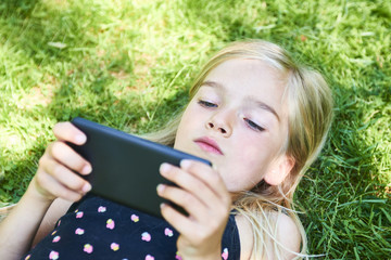  Blond child girl outdoors playing games with a mobile phone

