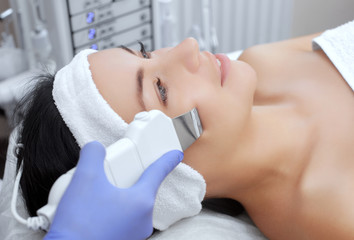 The doctor-cosmetologist makes the apparatus a procedure of ultrasound cleaning of the facial skin of a beautiful, young woman in a beauty salon. Cosmetology and professional skin care.