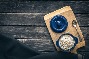 Barley porridge in the blue ceramic pot on dark aged wooden background. Healthy breakfast.