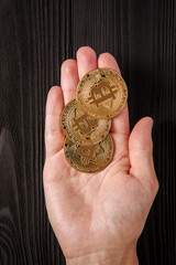 gold bitcoin in hands at the woman against the background of a wooden table