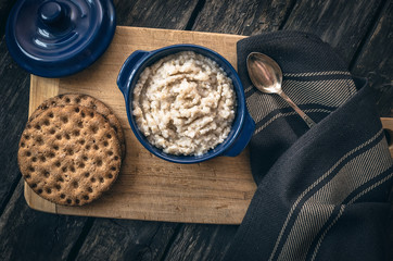 Barley porridge in the blue ceramic pot and bread on dark aged wooden background. Healthy breakfast.