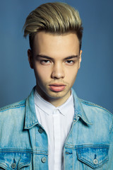 portrait of multiracial handsome man wearing jeans jacket and white shirt on blue wall background,