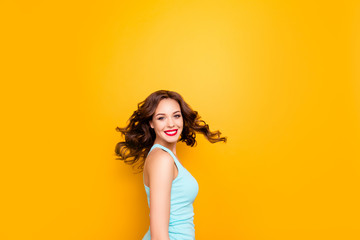 Portrait of excited playful girl turning with flying hair looking at camera enjoying summer time isolated on yellow background