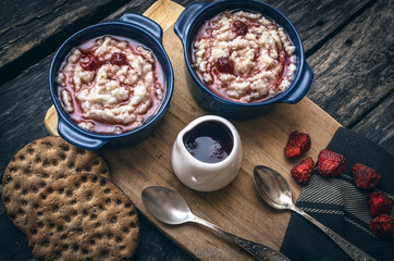 Barley porridge with strawberry jam in the blue ceramic pot and bread on dark aged wooden background. Healthy breakfast.