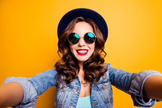 Self portrait of positive toothy girl shooting selfie on front camera with two hands having red lipstick beaming smile modern hairdo isolated on yellow background, photography concept