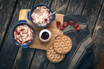 Barley porridge with strawberry jam in the blue ceramic pot and bread on dark aged wooden background. Healthy breakfast.