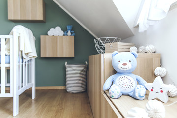 Stylish scandinavian newborn baby room with toys, teddy bear, mock up photo frame. Modern green background wall. 