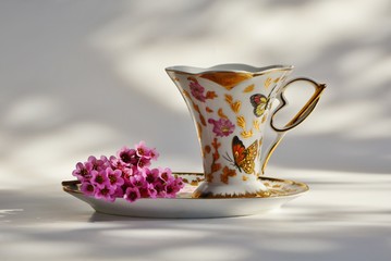 Elegant сup and saucer with a small bouquet of pink flowers on a white background.