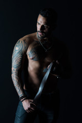 Obraz na płótnie Canvas Man with tattoo design on skin. Bearded man with muscular torso. Fashion model with leather belt in jeans. Sportsman with tattooed arm and chest. Bodycare with fitness and sport
