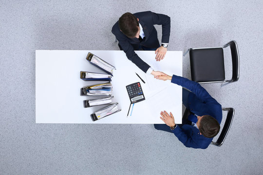 Two businessmen shaking hands while sitting at the table, view from above. Bookkeeper or financial inspector  making report, calculating or checking balance