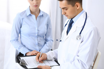 Male doctor holding application form while consulting female patient in hospital office. Perfect...