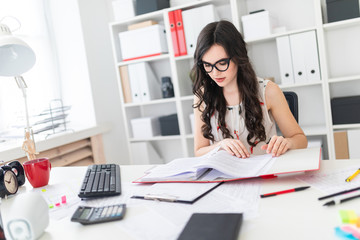 Beautiful young girl sits at office desk and scrolls through a folder with documents.