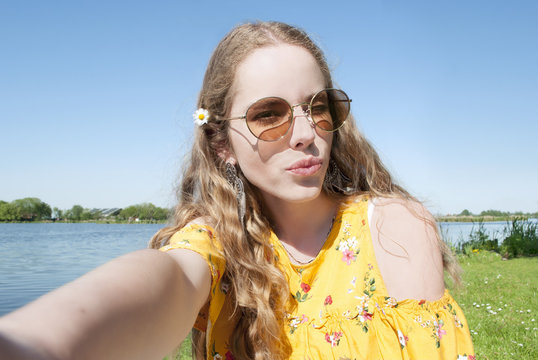 beautiful young millennial girl, taking selfie pcture with cell phone camera, outdoors in park on sunny day