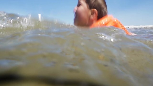 boy in lifejacket swim in sea with waves