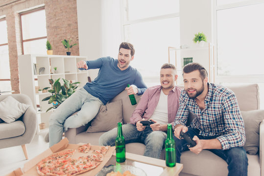 Three attractive, handsome, stylish, emotional men playing video game, worry, cheer, pointing forefinger, having pizza, lager, alcohol sitting in living room