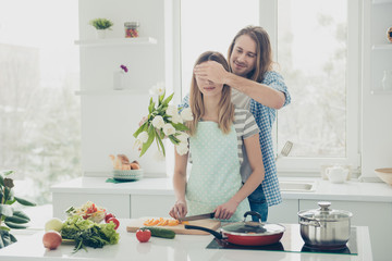 Portrait of handsome man closing eye with palm to lover preparing bouquet of white flowers while woman making vegan salad keeping healthy nutrition diet meal