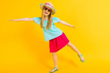 Girl with red hair on a yellow background. A charming girl in bright summer clothes pulled her hands out to the sides.