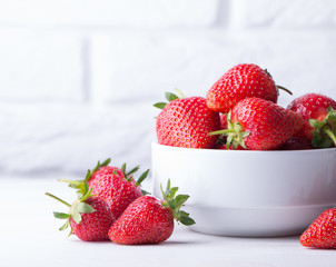 Heap of fresh strawberries in ceramic bowl on rustic white wooden background