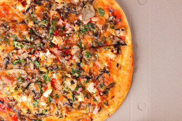 Pizza in a box on a wooden background. Italian pizza with chicken, mushrooms, greens, cheese and sauce. Festive meal in a cardboard box. Copy space