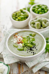Broad bean soup with fresh mint and feta cheese in a white bowl on a wooden table. Healthy and delicious vegetarian food