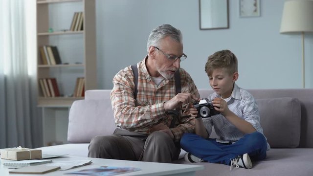 Grandpa explaining grandson how to use retro camera, young photographer dreams