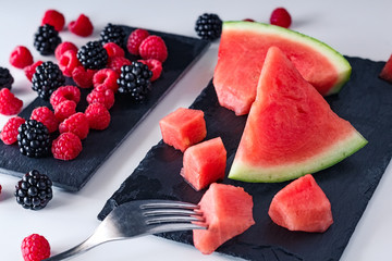 Closeup of a composition of fresh summer fruit, watermelon, raspberries and blackberries on white background with slate. Mediterranean diet with varied summer fruits. Stock photo. Top front View