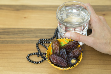 Date fruits in the plate and a glass of water and hand on the wooden background for eleven month...