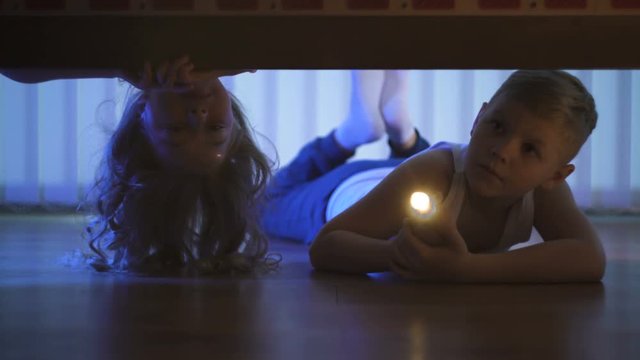 The kids with a flashlight looking under the bed. evening night time