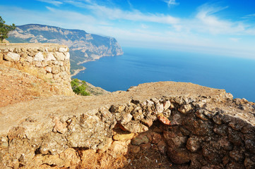 Old barrier and view of coast with mountains and forest, blue sea and sky with clouds