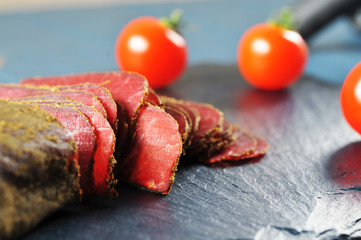 Close-up of sliced meat and tomatoes on the dark board and blue background