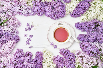 Lilac flowers background with cup of black tea in the middle. Copy space, top view. Spring background.