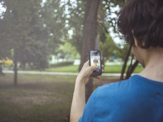 cute teenager boy takes self portrait in the public park with modern phone