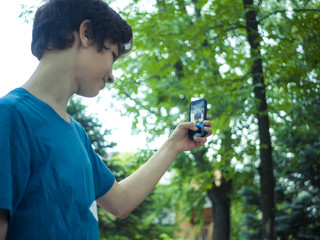 cute teenager boy takes self portrait in the public park with modern phone