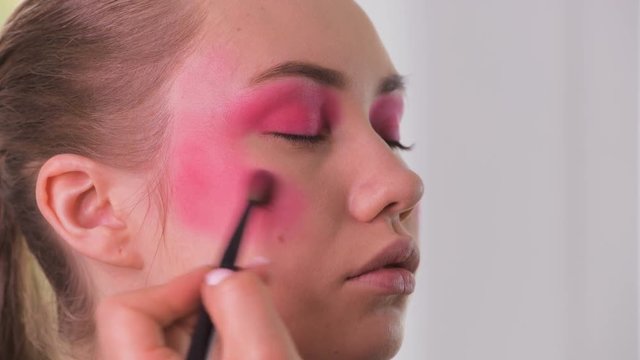Eye makeup artist applying and feathering eyeshadow powder. Beautiful woman model face. Close-up.