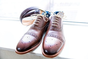Men's new leather brown shoes closeup still life isolated with blue polka dot socks, watch, shoelaces laces tied, wedding or interview preparation, belt on windowsill in room