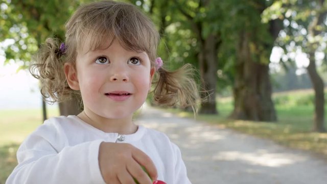 Slow motion, portrait playful baby daughter blowing soap bubbles during fun family trip to the park