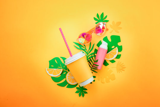 Summer vacation flat lay with tropical leaves, a refreshing drink, sunglasses, sunscreen on a sunny yellow background with copy space