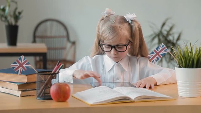 Smart girl in glasses and neat white blouse using tablet, having entertaining and relaxing break during English classes, indoor shot in private language school