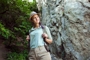 Girl traveler walks through the mountains and woods. He smiles. Green shirt shorts and tan. Straw hat. Photographer is a tourist researcher.