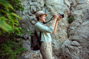 Girl traveler walks through the mountains and woods. He smiles. Green shirt shorts and tan. Straw hat. Photographer is a tourist researcher.