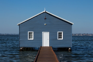 Blue wooden boatshed surrounded by water against clear blue sky