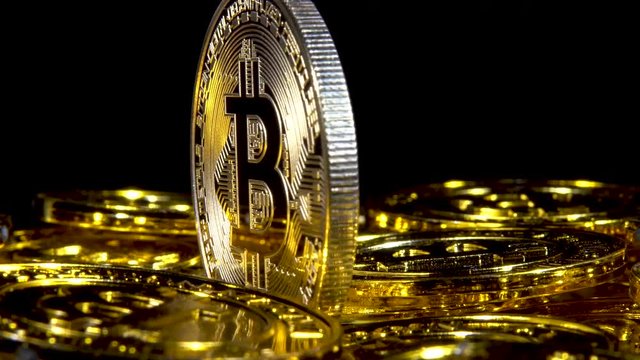 Fast rotation low angle extreme closeup of a Bitcoin amid a sea of bitcoins on a black background.