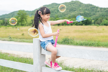 A little girl blowing soap bubbles in summer park. Background toninf for instagram filter.