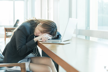 tired businesswoman sleeping with her computer on the desk while sitting near the window