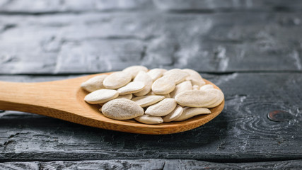 A spoon with pumpkin seeds on a dark rustic table.