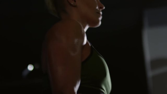 Closeup of sexy muscular woman in sports bra doing dumbbell curls while working out in dark gym