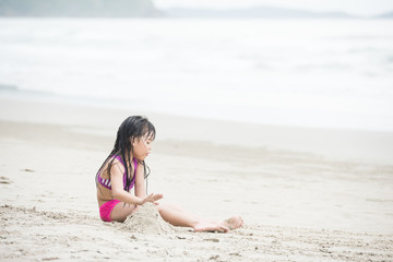 Happy child playing with sand at the beach in summer