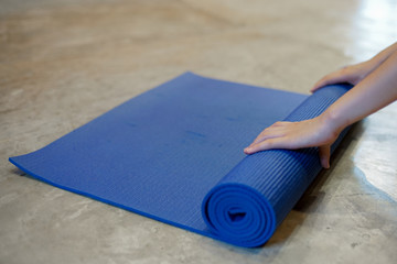 young yoga woman rolling her mat after a yoga class on polished concrete floor close up