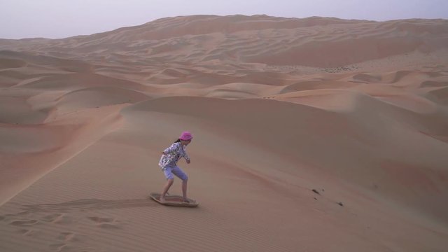 Teenage girl rolls on sandboard on the slope of a dune in the Rub al Khali desert United Arab Emirates stock footage video